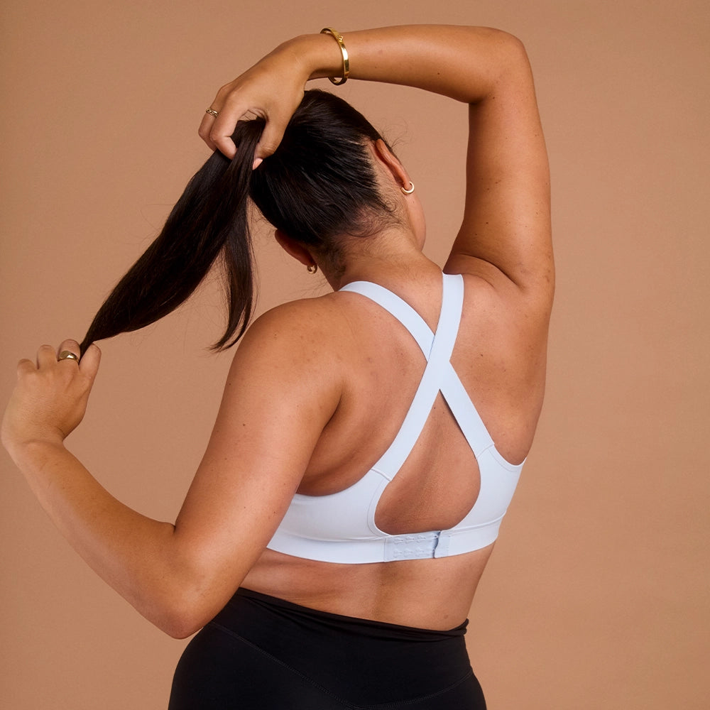 Woman in light blue cross-back sports bra holding her ponytail