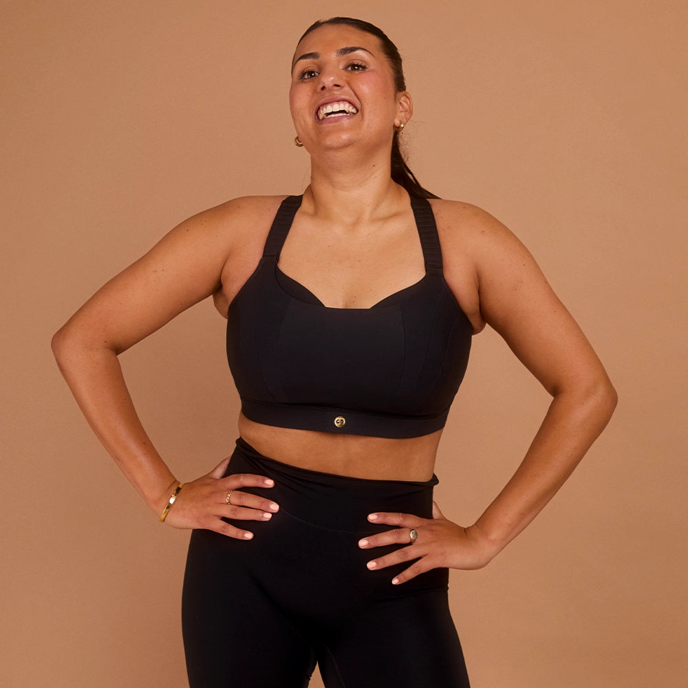 Smiling woman with hands on hips wearing black high impact sports bra and leggings