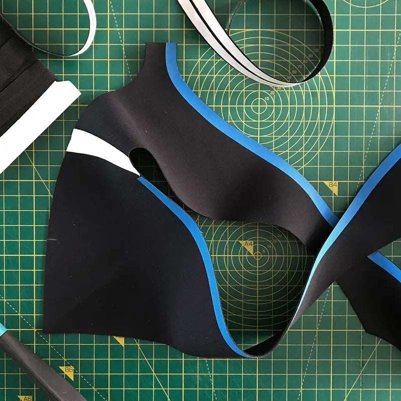 Black sports bra pieces and elastic trims laid out on a green cutting mat for construction.