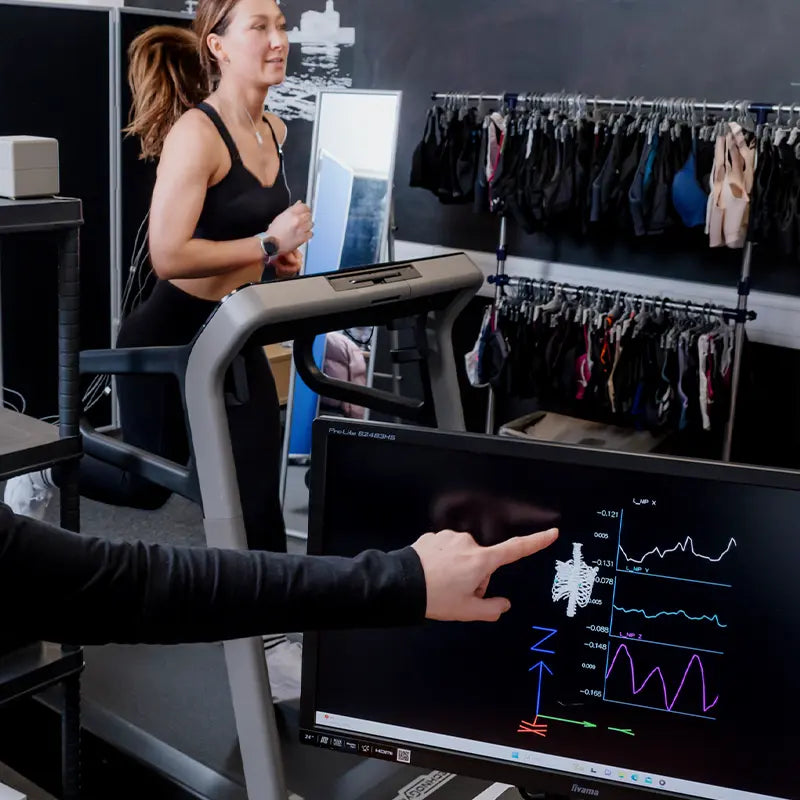 Woman running on treadmill while sports bra performance is monitored on a screen.