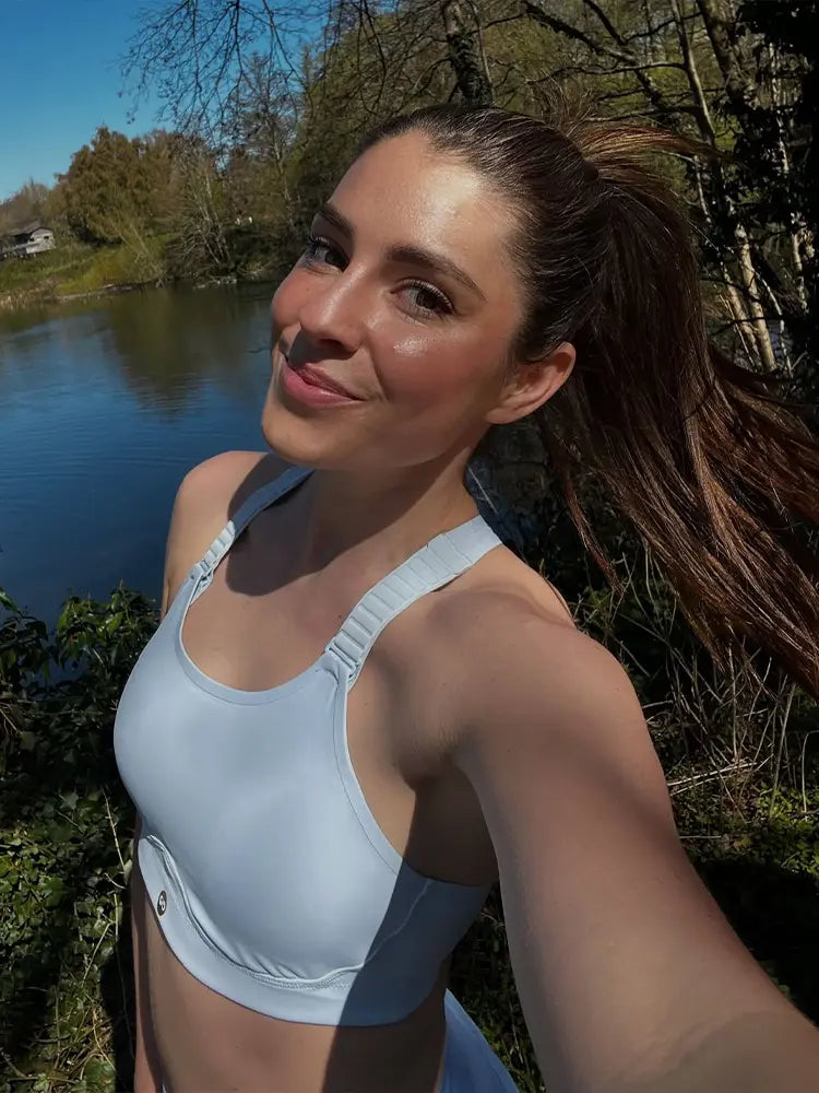Woman smiling in blue sports bra, taking selfie while running.