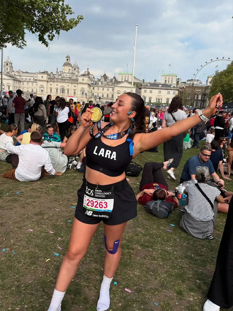 Runner Lara Potter celebrating marathon finish in black sports bra and medal.