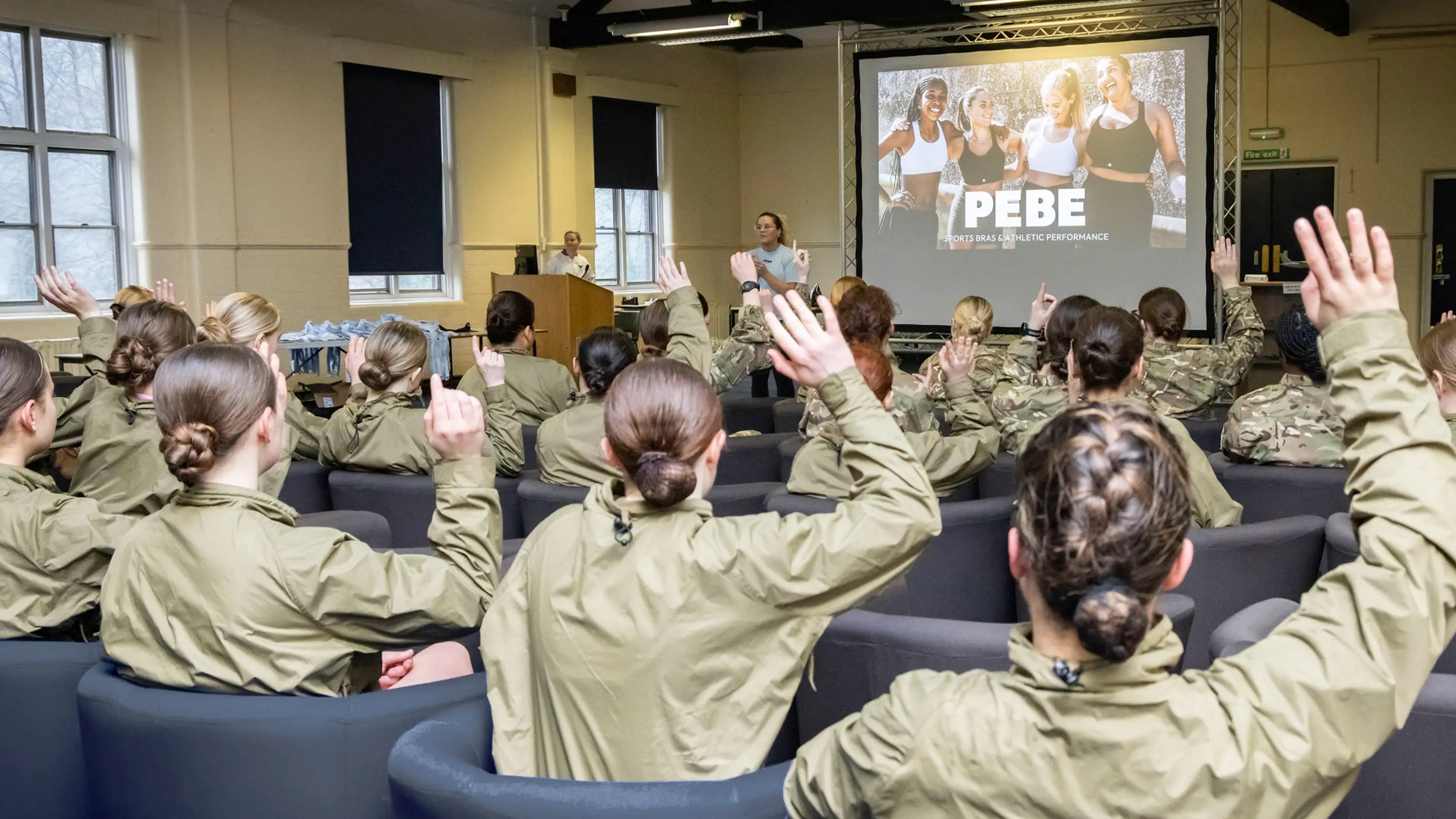 Female military personnel attending PEBE sports bra education workshop, engaging with presenter about proper fit and performance