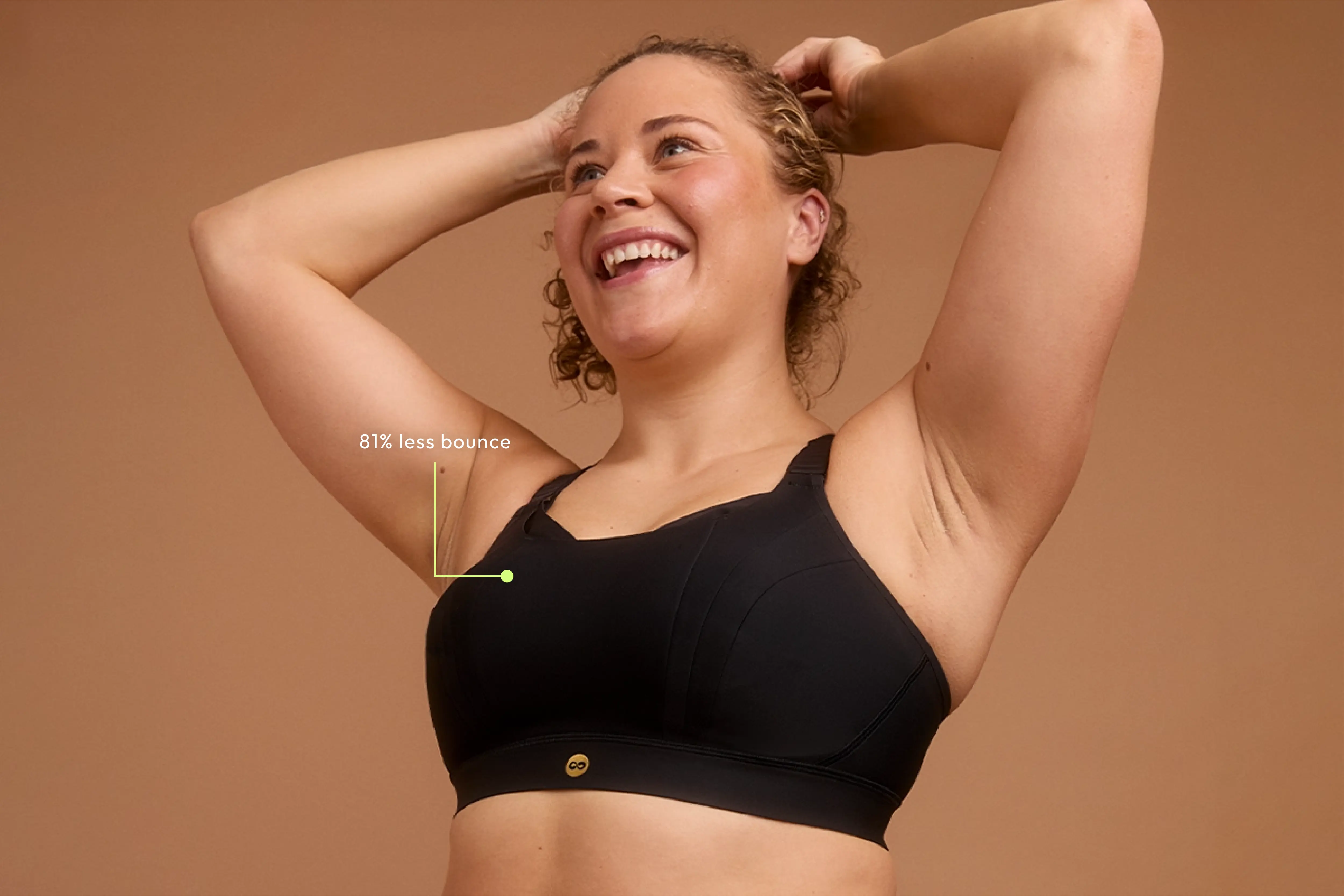 Woman smiling in black sports bra, arms raised, showing 81% less bounce feature.