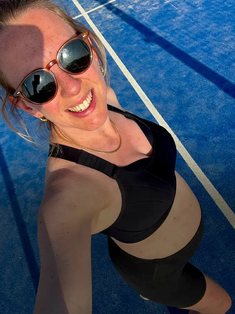 Woman in black sports bra smiling on blue running track in the sun.