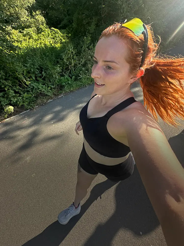 Woman with red hair running outdoors in black sports bra and sunglasses.