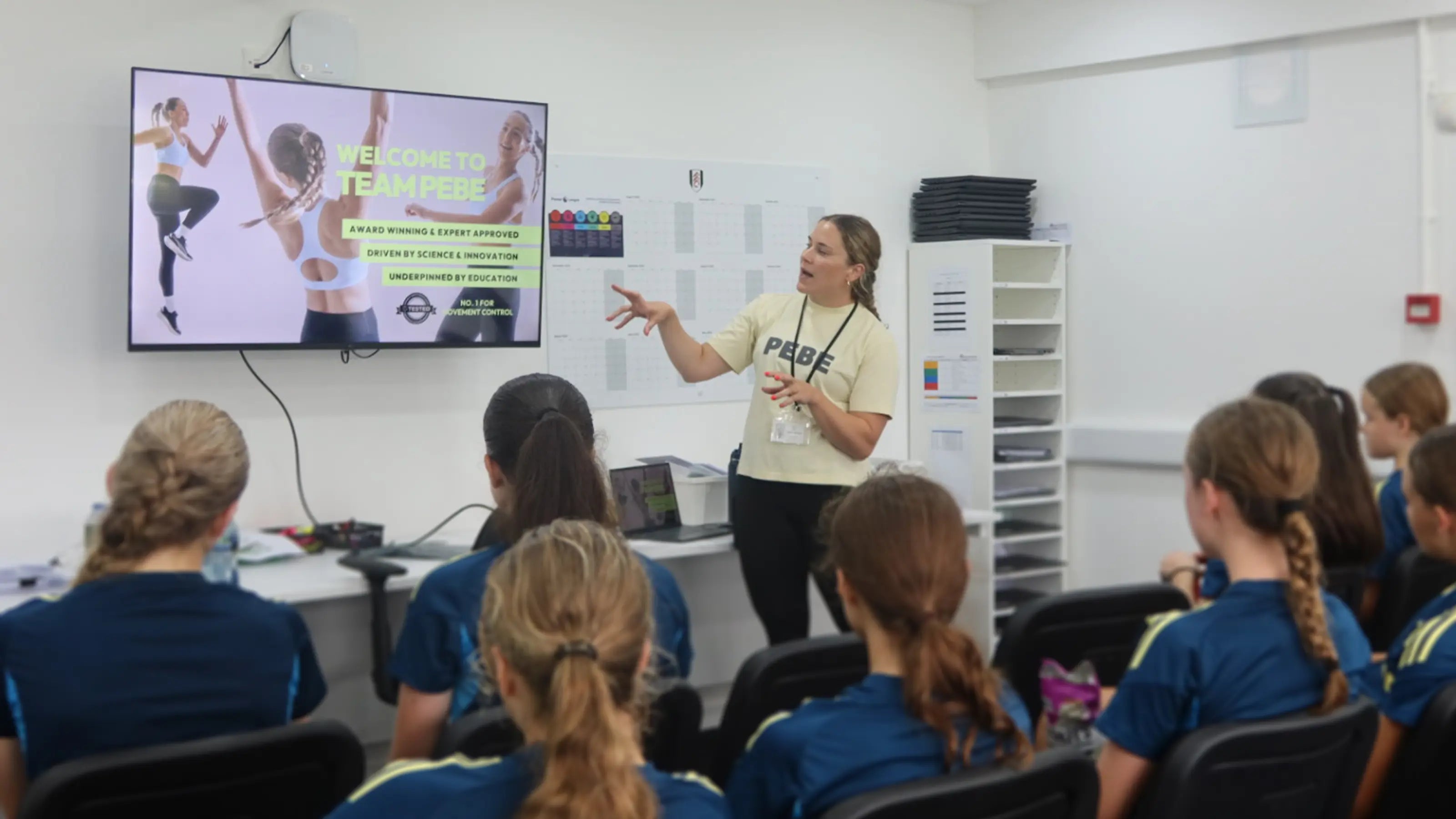 Coach in PEBE T-shirt presenting sports bra education session to a group of students.